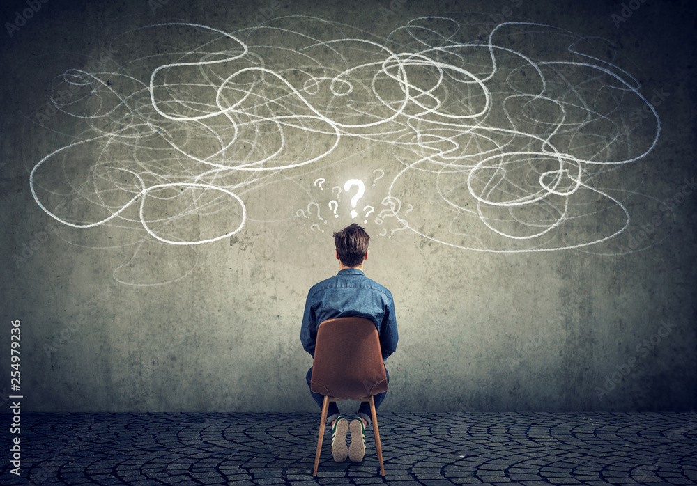 businessman sitting on chair looking at a scribble on a wall feeling confused